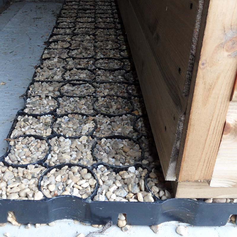 Row of small stones in black plastic containers next to a wooden structure